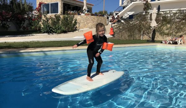 Kid is having fun on a surfboard in the pool while the family is watching